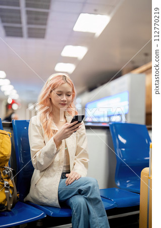 Happy asian tourist woman using mobile smartphone with suitcase traveling between waits for flight in Airport Terminal, flight check in, Tourist journey trip concept 112770219