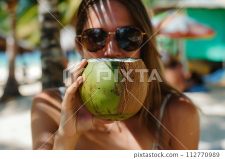 Young female sips a coconut drink under palm trees, embodying vacation vibes 112770989
