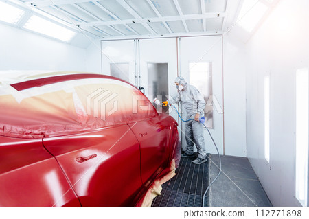 Wide angle of automobile repairman painter in protective workwear and respirator painting car body in paint chamber. 112771898