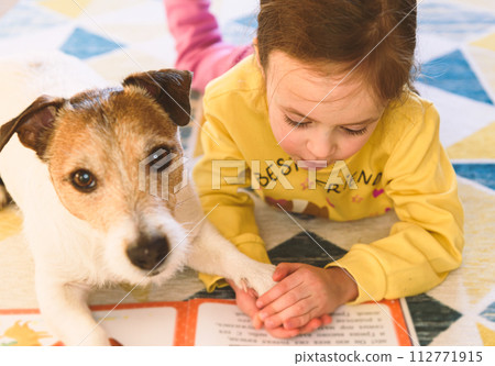 Small girl learning to read. Kid is reading a book to her pet dog. Small girl learning to read. Kid is reading a book to her pet dog. 112771915