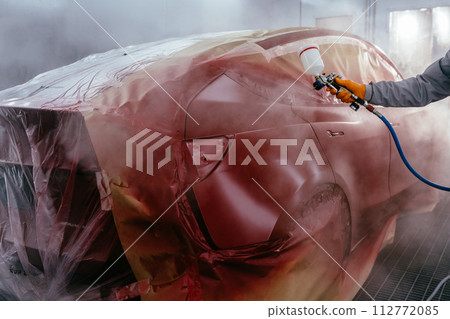 Unrecognizable man with protective clothes and mask painting car using compressor. Automotive paint services, quality auto body shop concept. Unrecognizable man with protective clothes and mask painting car using compressor. Automotive paint services, quality auto body shop concept. 112772085