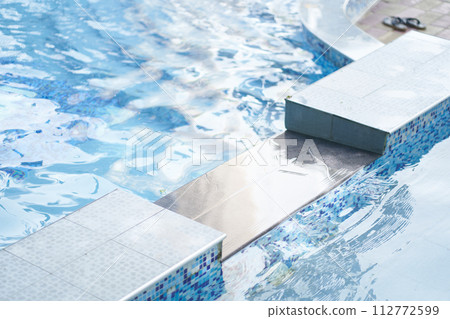 Part of swimming pool with blue mosaic ceramic tiles, with blue water, squared tiles, water surface, ripple. Background with copy space. Concept of summer, swimming, leisure time, vacation. 112772599