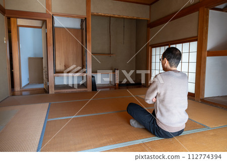 A middle-aged man sits in a Japanese-style room deep in thought after sorting through the belongings of his parents' house and carrying out all the belongings inside. 112774394