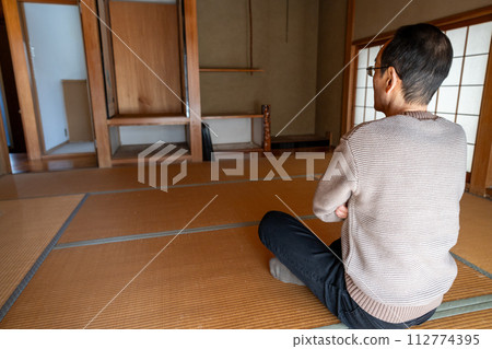 一名中年男子整理父母家的物品，將裡面的物品全部搬了出來，坐在日式房間裡陷入沉思。 112774395