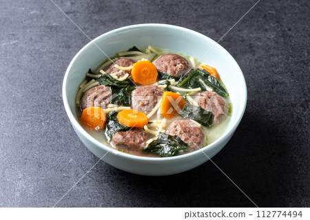 Italian Wedding Soup with meatballs and spinach on black slate background 112774494