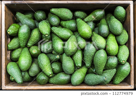 Avocado in the supermarket. Green ripe avocado background on the farm. Fruit and vegetable industry, vegetarian food. 112774979