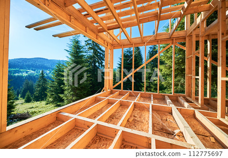 Wooden frame house under construction near forest. Beginning of new construction of cozy house on the edge of forest in mountains. Concept of modern ecological construction and modern architecture. Wooden frame house under construction near forest. Beginning of new construction of cozy house on the edge of forest in mountains. Concept of modern ecological construction and modern architecture. 112775697