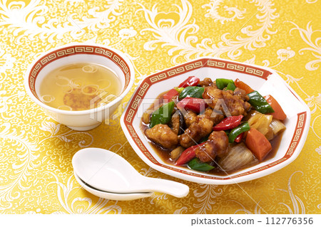 糖醋肉是一道經典的中國菜餚，盛在八角形的盤子上，上面覆蓋著黃色的中國圖案布。 112776356