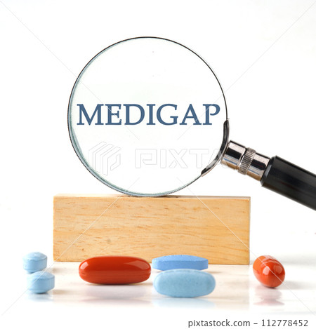 Medical concept. MEDIGAP through a magnifying glass on a wooden block with vitamins, pills in the foreground Medical concept. MEDIGAP through a magnifying glass on a wooden block with vitamins, pills in the foreground 112778452