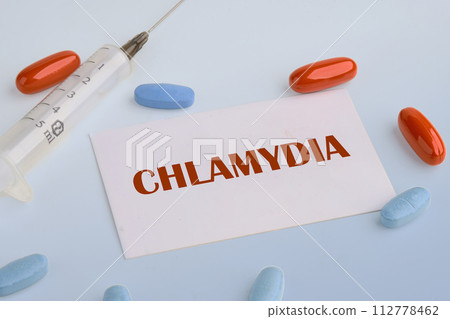 Medical concept. Word Chlamydia. on a white business card on a blue background next to a syringe, pills, vitamins 112778462
