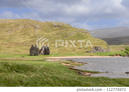 In Scottish Highlands, weathered Calda House ruins stand, surrounded by verdant fields and hills 112778972
