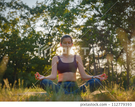 Young asian woman doing meditation in morning or evening at park, healthy woman relaxing and practicing yoga at city park. Mindfulness, destress, Healthy habits and balance concept 112779393