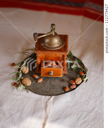 Retro coffee grinder on table with nuts and olive branch over beautiful old linen tablecloth Retro coffee grinder on table with nuts and olive branch over beautiful old linen tablecloth 112779427