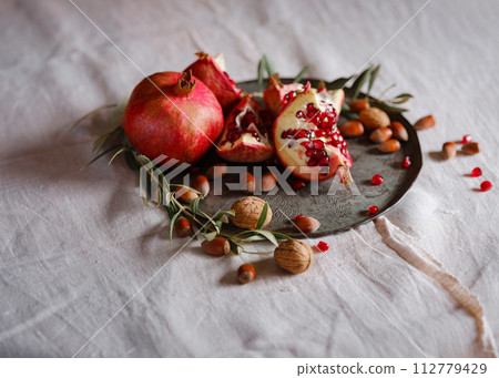 Image of Still Life with Turkish Pomegranate and olive branch on old retro plate. Dark wood background, antique copper plate. Fresh ripe whole pomegranates, opened pomegranate and seeds Image of Still Life with Turkish Pomegranate and olive branch on old retro plate. Dark wood background, antique copper plate. Fresh ripe whole pomegranates, opened pomegranate and seeds 112779429