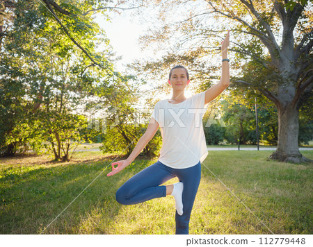 Young asian woman doing yoga in morning or evening at park, healthy woman relaxing and practicing tree pose at city park. Mindfulness, destress, Healthy habits and balance concept Young asian woman doing yoga in morning or evening at park, healthy woman relaxing and practicing tree pose at city park. Mindfulness, destress, Healthy habits and balance concept 112779448