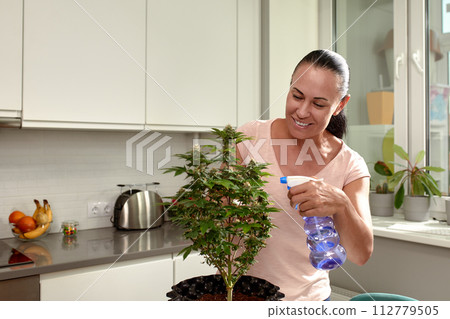 Smiling woman caring for houseplant in a bright kitchen setting Smiling woman caring for houseplant in a bright kitchen setting 112779505