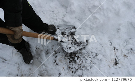 View from the upper angle to clean the large layer of snow with a shovel in the hands of a man in black winter clothes, the removal of snowdrifts in the garden or yard after abundant snowfall 112779670