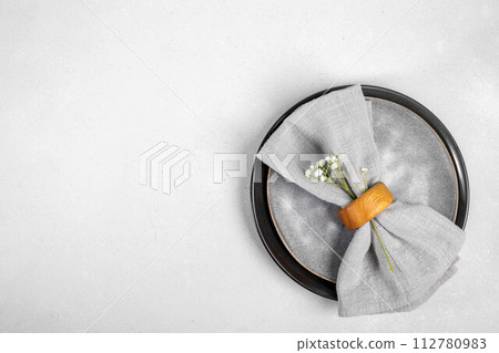 Table serving in gray tones. Gray napkin on stylish plates on gray background. Top view. Copy space. Table serving in gray tones. Gray napkin on stylish plates on gray background. Top view. Copy space. 112780983