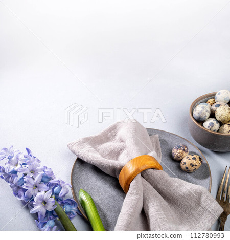 Easter table serving. Gray tableware, gray napkin, quail eggs, jacinth flower on neutral. Copy space Easter table serving. Gray tableware, gray napkin, quail eggs, jacinth flower on neutral. Copy space 112780993
