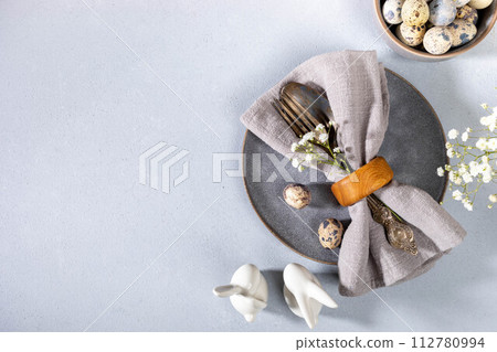 Napkin, vintage cutlery, quail eggs, gray plate, flowers, ceramic bunnies. Gray Easter table setting 112780994
