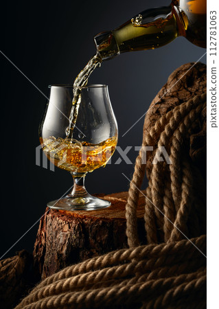 Brandy is poured from a bottle into a glass. Brandy is poured from a bottle into a glass. 112781063