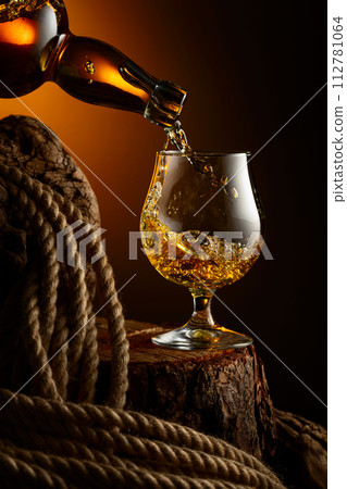 Brandy is poured from a bottle into a glass. Brandy is poured from a bottle into a glass. 112781064