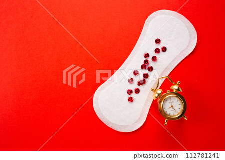 Alarm clock and feminine hygiene pad with red glitter on red background. First menstrual period concept 112781241