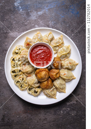 Uzbek samsas and manti with meat, pumpkin and greens on a plate with red sauce 112782014