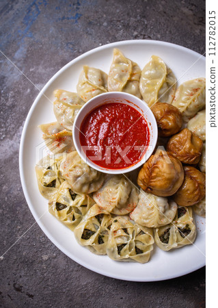 Uzbek samsas and manti with meat, pumpkin and greens on a plate with red sauce 112782015