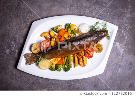 Trout fish with grilled vegetables on a white plate. Isolated on a black background. 112782016