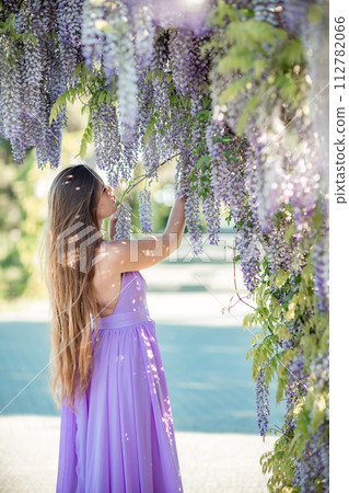 Woman wisteria lilac dress. Thoughtful happy mature woman in purple dress surrounded by chinese wisteria 112782066