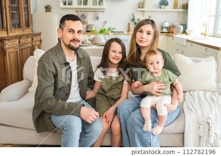Happy family at home. Mother father two children daughters relaxing on sofa indoor. Mom dad parents baby girls kids relax playing having fun together. Family smiling laughing enjoying tender moment Happy family at home. Mother father two children daughters relaxing on sofa indoor. Mom dad parents baby girls kids relax playing having fun together. Family smiling laughing enjoying tender moment 112782196