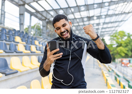 Energetic athlete enjoying victory with a fist pump in an empty stadium, showing determination and success. Energetic athlete enjoying victory with a fist pump in an empty stadium, showing determination and success. 112782327