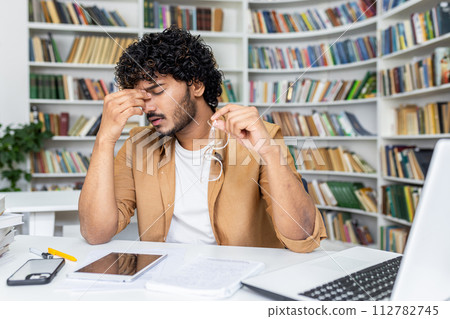 Tired muslim man taking of glasses and rubbing eyes with closed eyes while working by laptop. Stressed retired manager waiting for break while having vision struggles due to long screen time. Tired muslim man taking of glasses and rubbing eyes with closed eyes while working by laptop. Stressed retired manager waiting for break while having vision struggles due to long screen time. 112782745