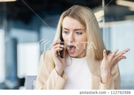 Worried female professional in conversation on mobile phone, expressing confusion and shock in corporate environment. 112782986