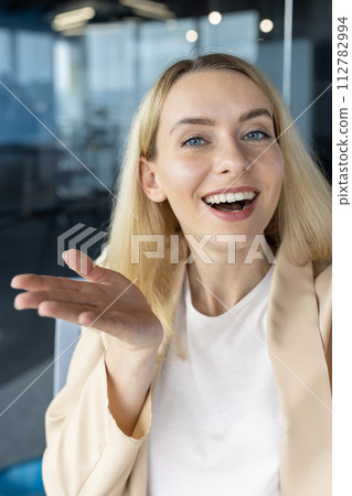 Cheerful blonde businesswoman speaking and gesturing, as if in a friendly discussion in a modern office setting. Cheerful blonde businesswoman speaking and gesturing, as if in a friendly discussion in a modern office setting. 112782994