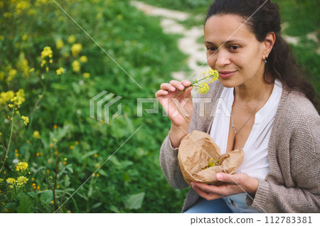 Beautiful smiling young woman collecting eco friendly medicinal herbs. Alternative medicine, naturopathy, herbal medicine 112783381