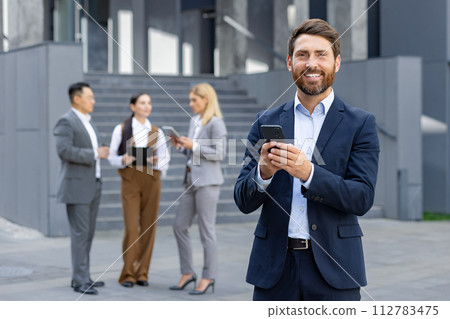 Corporate professionals engaged with smartphones during a break outside modern office building, depicting connectivity and business communication. 112783475