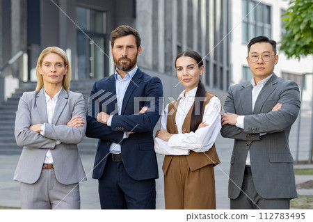 Four professional business individuals posing confidently outdoors, displaying teamwork and corporate success in a modern urban setting. 112783495