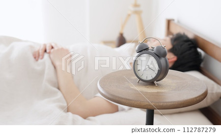 A man sets an alarm clock and sleeps 112787279