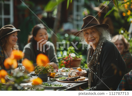 A joyful senior grandmother sits surrounded by her family at an outdoor dinner table. Celebrates the importance of family bonds and intergenerational connections. Generative AI. A joyful senior grandmother sits surrounded by her family at an outdoor dinner table. Celebrates the importance of family bonds and intergenerational connections. Generative AI. 112787713