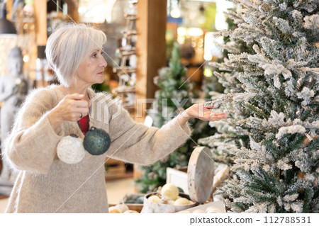 Mature woman purchasing christmas toys and decorations at christmas fair shop Mature woman purchasing christmas toys and decorations at christmas fair shop 112788531