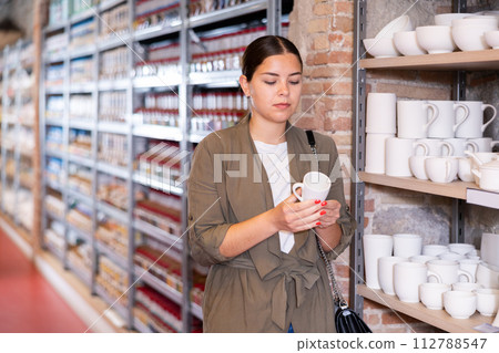 Positive woman chooses mug or cup in pottery and ceramics shop Positive woman chooses mug or cup in pottery and ceramics shop 112788547
