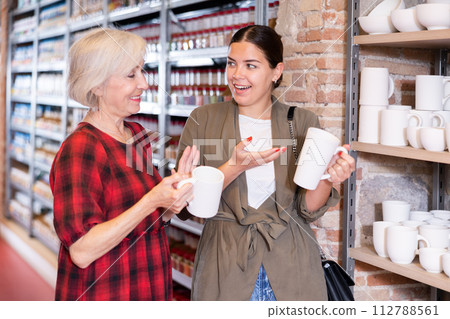 Two women choose mugs or cups together in pottery and ceramics shop 112788561