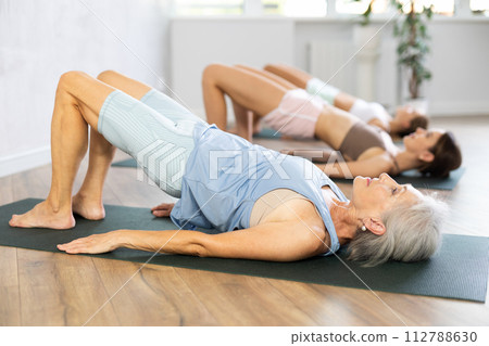Mom, grandma and teen daughter do half bridge Setu Bandha Sarvangasana, glute bridge pose 112788630