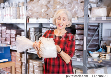 Elderly woman chooses pottery clay in shop 112788632