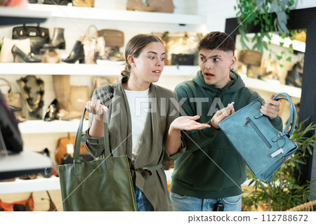 Young man with girl friend inspects shop window and is looking for modern handbag Young man with girl friend inspects shop window and is looking for modern handbag 112788672