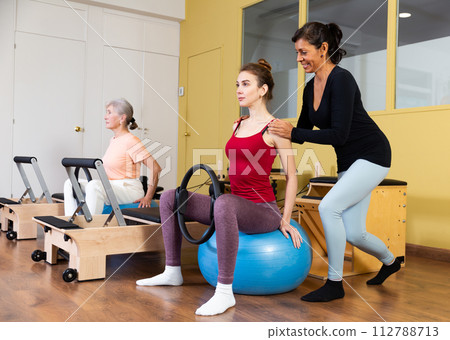 Latin american woman instructor helps to perform exercises with fitness balls and rings Latin american woman instructor helps to perform exercises with fitness balls and rings 112788713