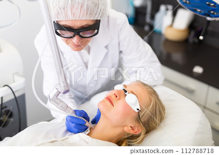 Cosmetologist using laser to resurface skin of young woman's face 112788718