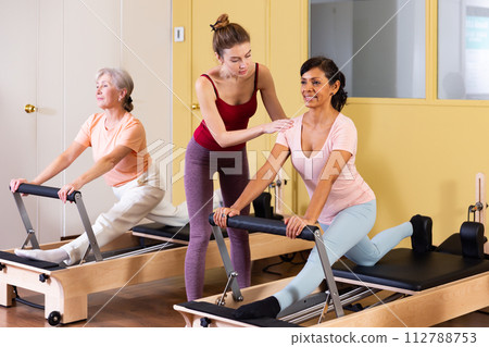 Two active women perform an exercise using a reformer bed Two active women perform an exercise using a reformer bed 112788753